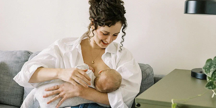 A smiling mom breastfeeding her baby while seated on the couch.