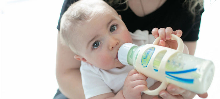 Infant being held and feeding from an ecru bottle with silicone handles