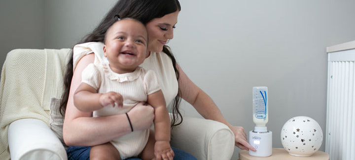 Mother using a bottle warmer while holding baby