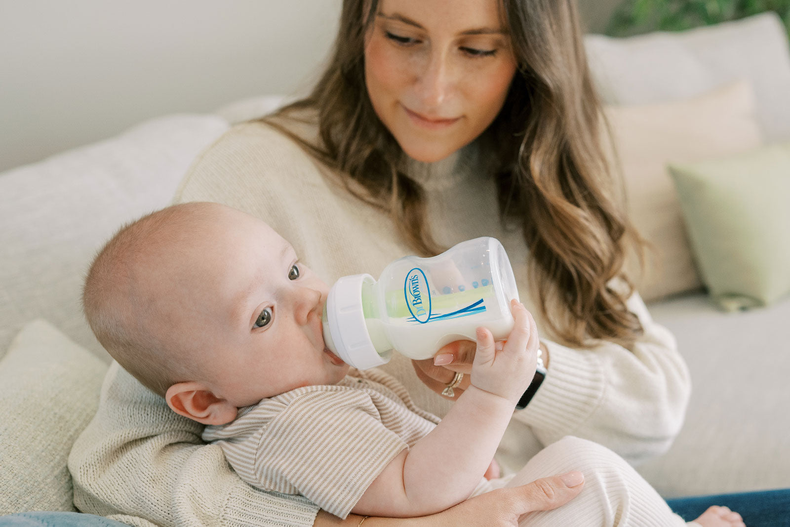 Woman holding a baby and feeding them from a bottle in a living room