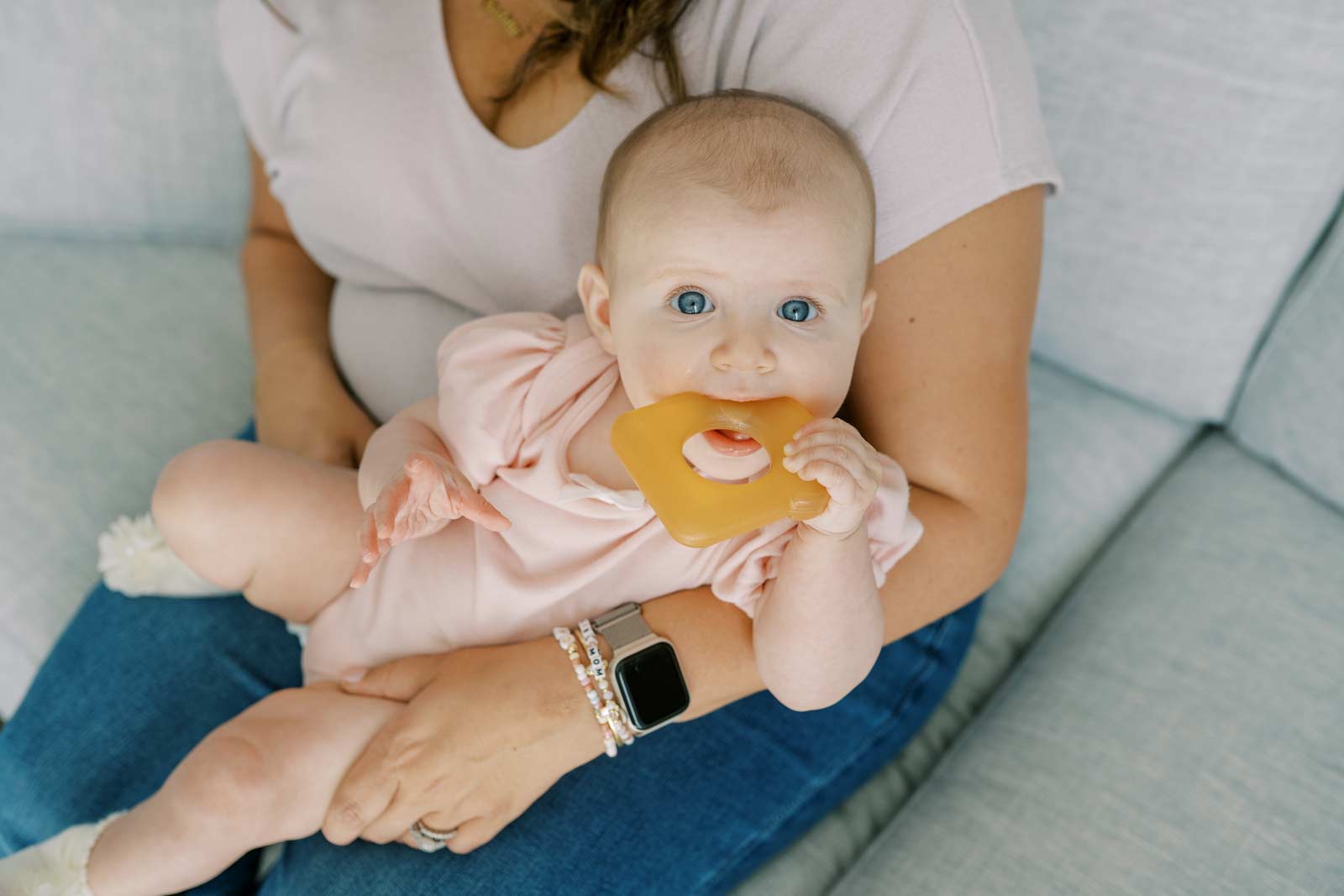 Baby sitting on her mom's lap chewing on a Dr. Brown's AquaCool Toast Teether