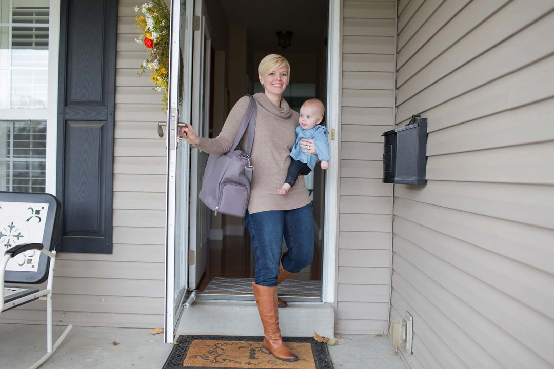 Mother walking out of home with Carryall bag and holding infant