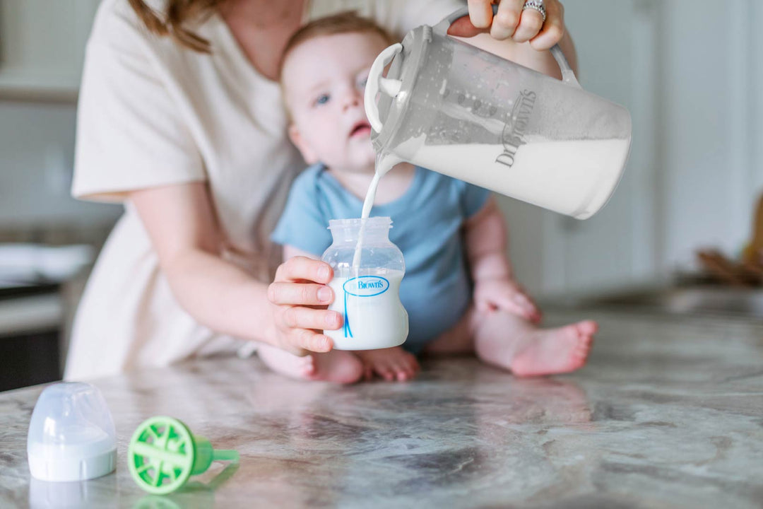 Baby sitting on counter as woman pours formula into bottle