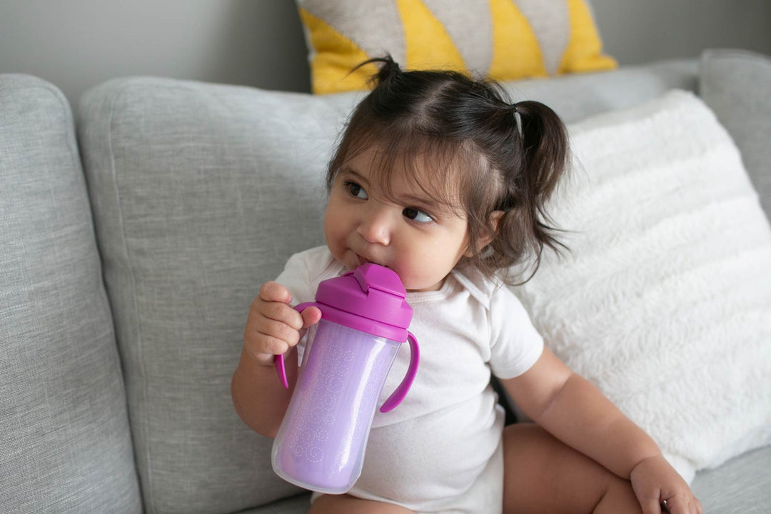 Child drinking from a purple sippy cup on a couch with pillows in the background