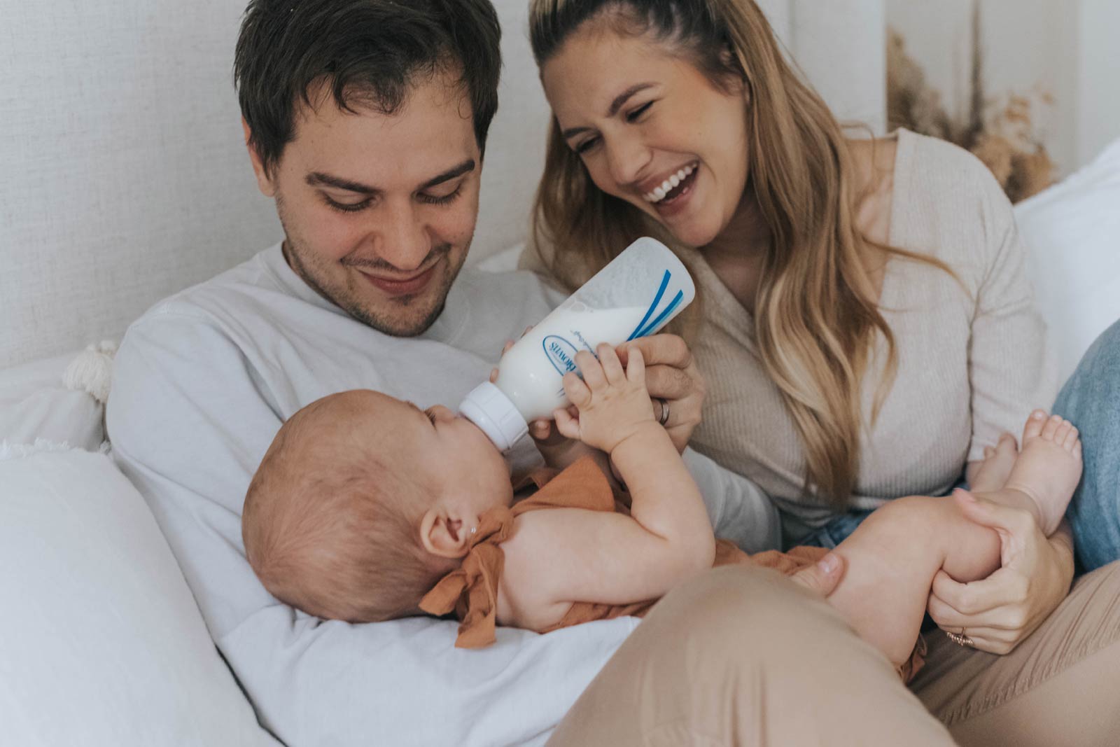 Mother and father feeding a baby with a bottle in a cozy indoor setting