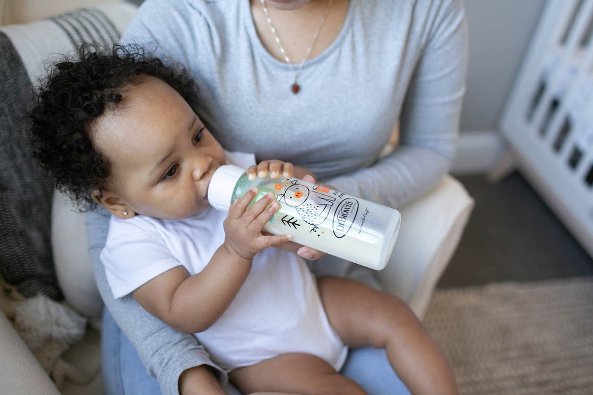 Baby sitting on adults lap and drinking from a bottle