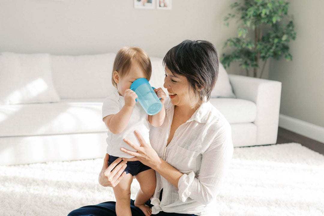 Woman holding toddler in living room as toddler drinks out of blue sippy cup