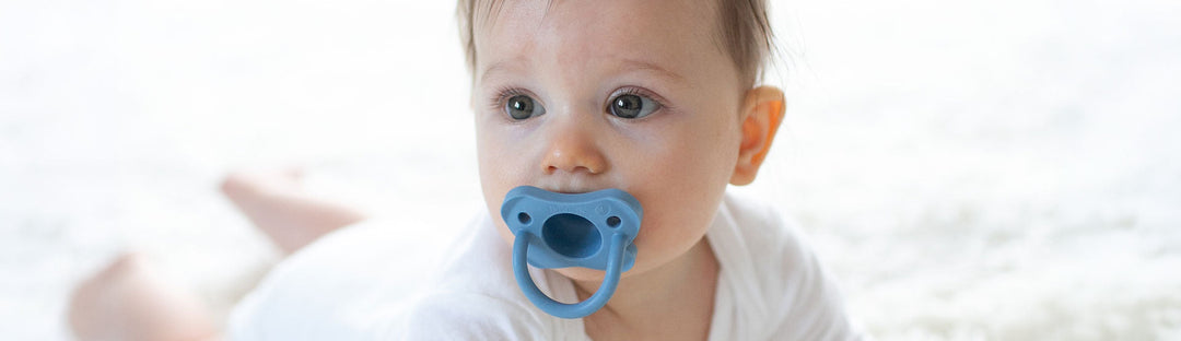 Dr. Brown's HappyPaci being used by a baby on a white rug.