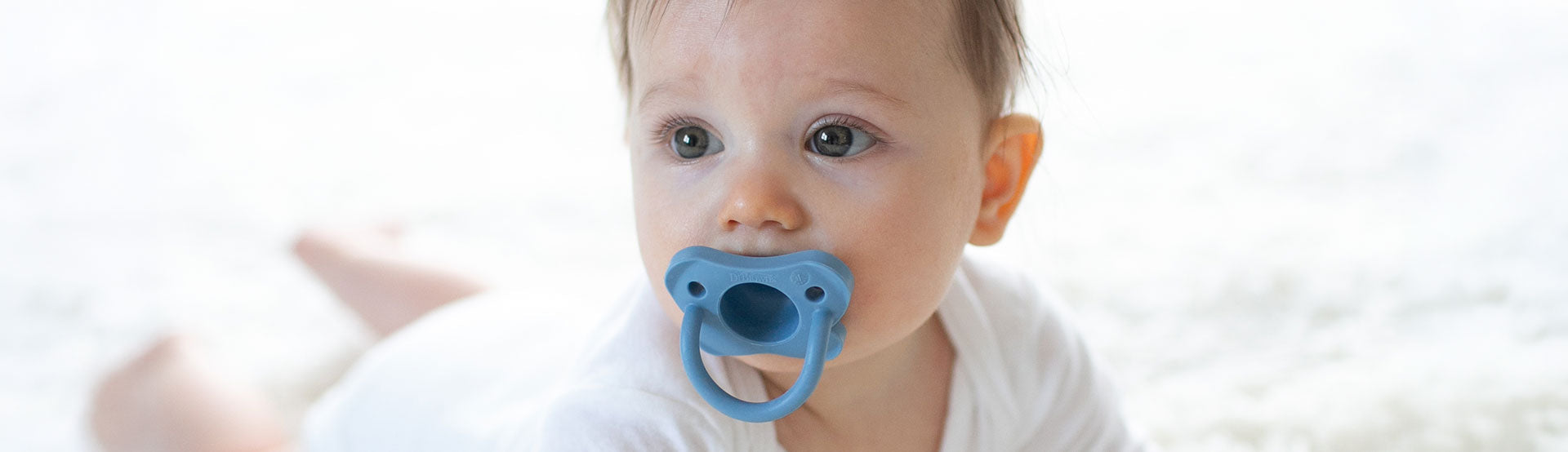 Dr. Brown's HappyPaci being used by a baby on a white rug.