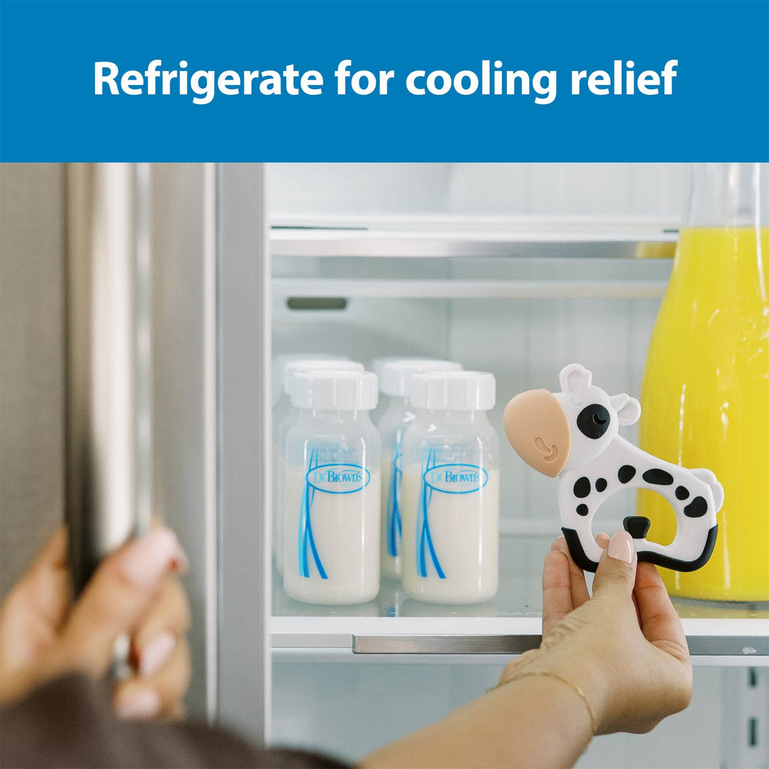 A person holds a cow-shaped refrigerator teether inside an open refrigerator shelf next to milk bottles and a yellow bottle, with the text 'Refrigerate for cooling relief' at the top.