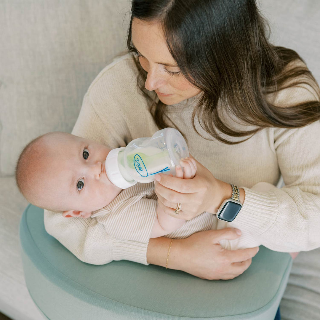 Woman feeding a baby with a bottle while sitting with a green Feeding and Nursing Lap Pillow on her lap
