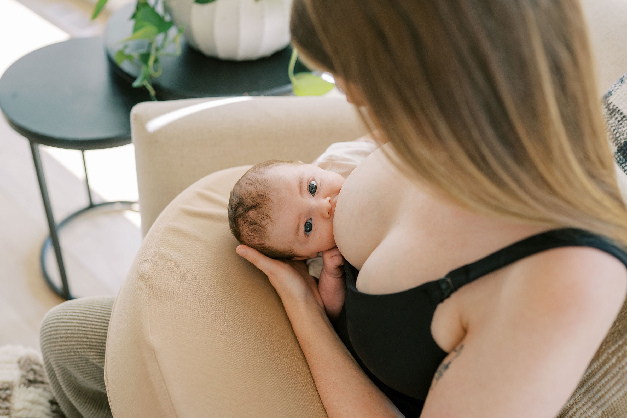 A mother in a black tank top breastfeeding a baby in a football hold on a Dr. Brown's™ Feeding & Nursing Lap Support Pillow