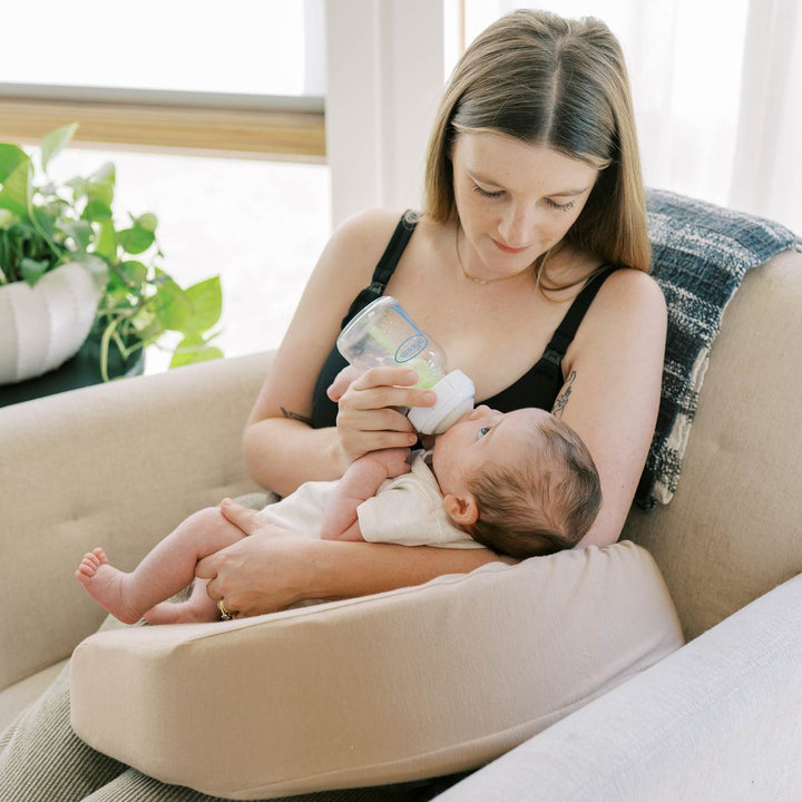 Woman feeding a baby with a bottle while sitting with a beige Feeding and Nursing Lap Pillow on her lap