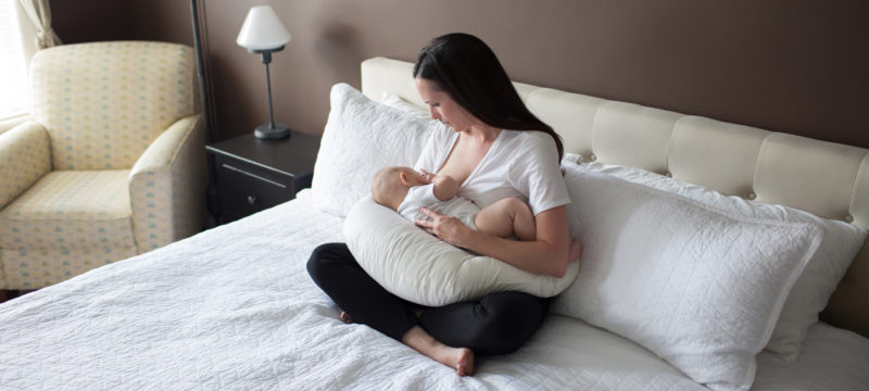 Woman sitting on bed breastfeeding baby