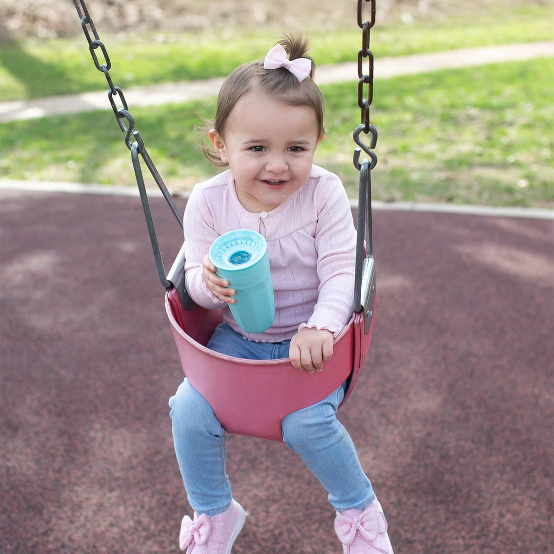 Child on a swing set holding a mint sippy cup in a park