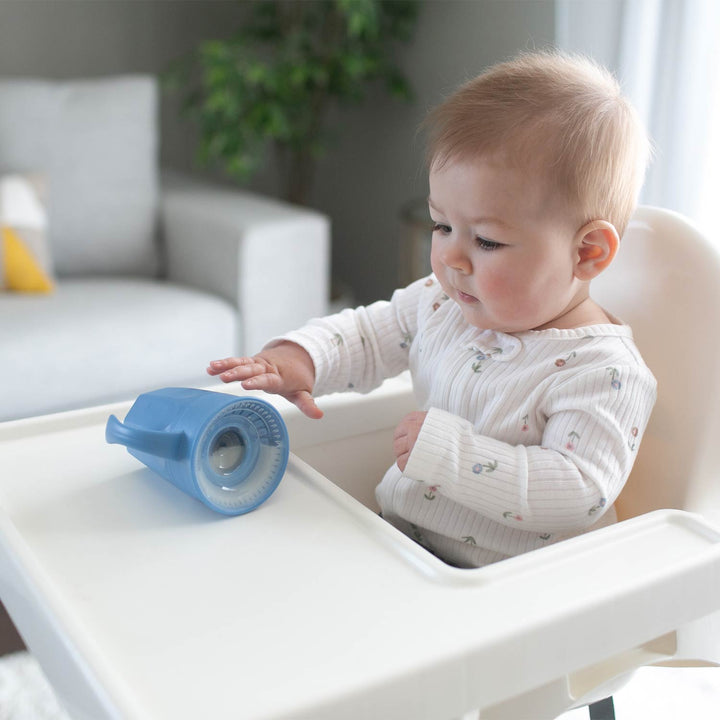 Baby in a high chair with a blue sippy cup on a tray