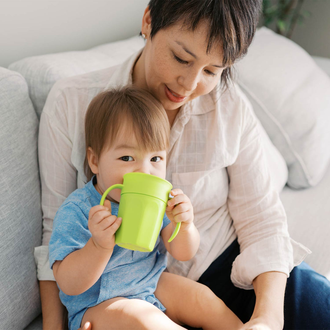 Woman and child sitting on a couch with the child holding a green Cheers360 cup.
