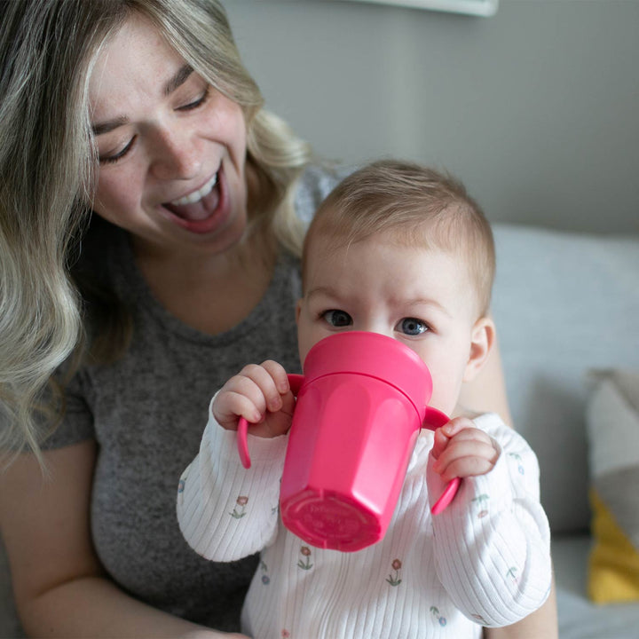 Mother holding baby drinking from a pink sippy cup