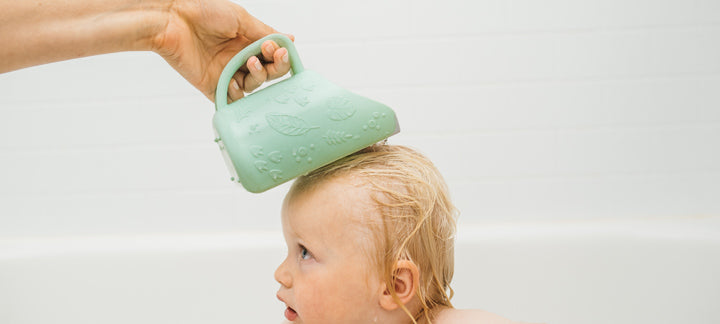 Baby being bathed with a green handheld rinse cup