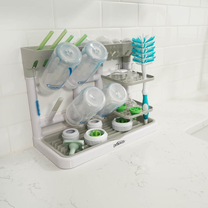 A Dr. Brown's gray baby bottle drying tower on a white marble countertop against a white subway tile backsplash.