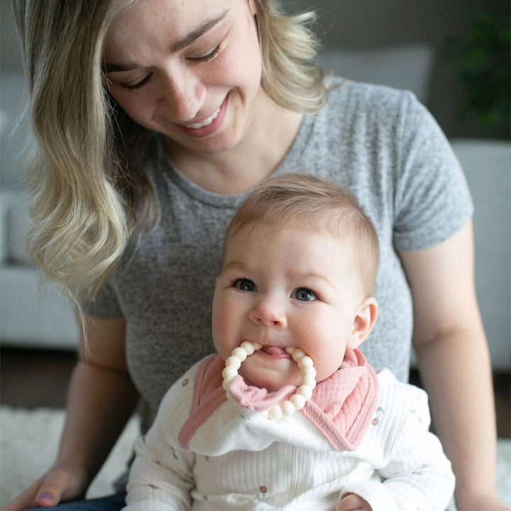 Parent sitting with infant teething on pink Muslin Bandana Bib