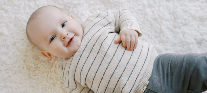 Baby lying on a carpet, wearing a striped outfit