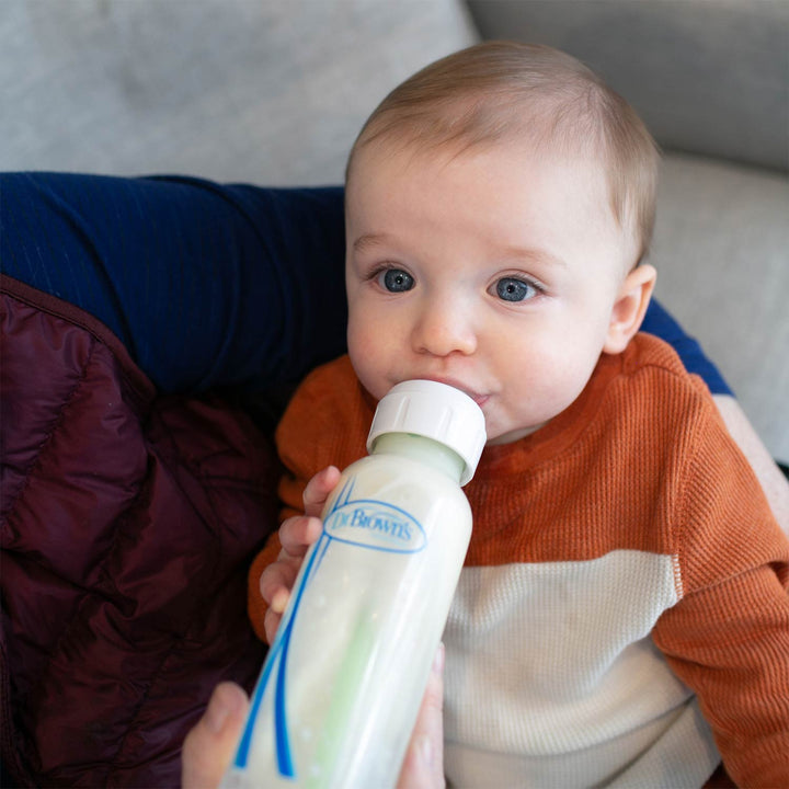 Baby drinking from a bottle held by an adult, with a focus on the bottle label.