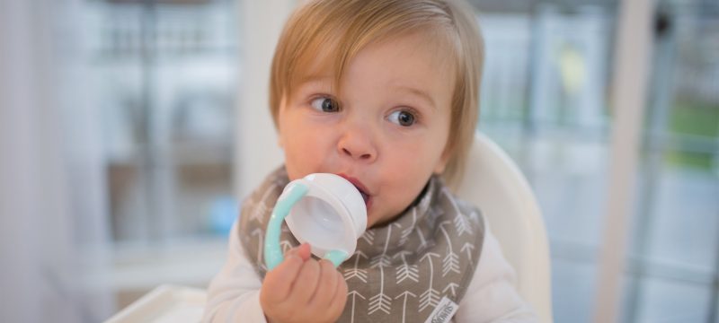 Baby sitting in high chair eating from silicone feeder