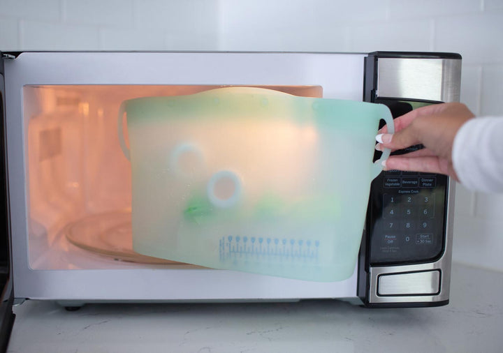 Person placing a green silicone sterilizer bag into a microwave.