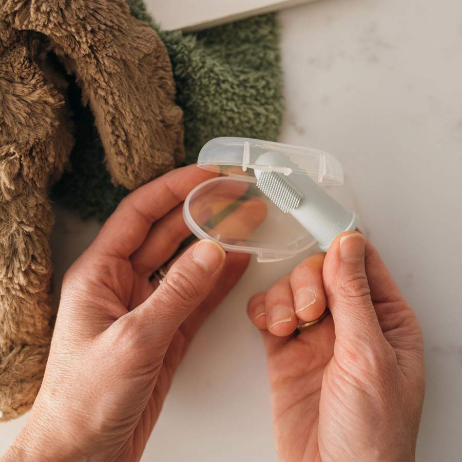 A person holds a safety razor with a white handle in a small transparent plastic case. A fuzzy brown and green towel is in the background on a white surface.