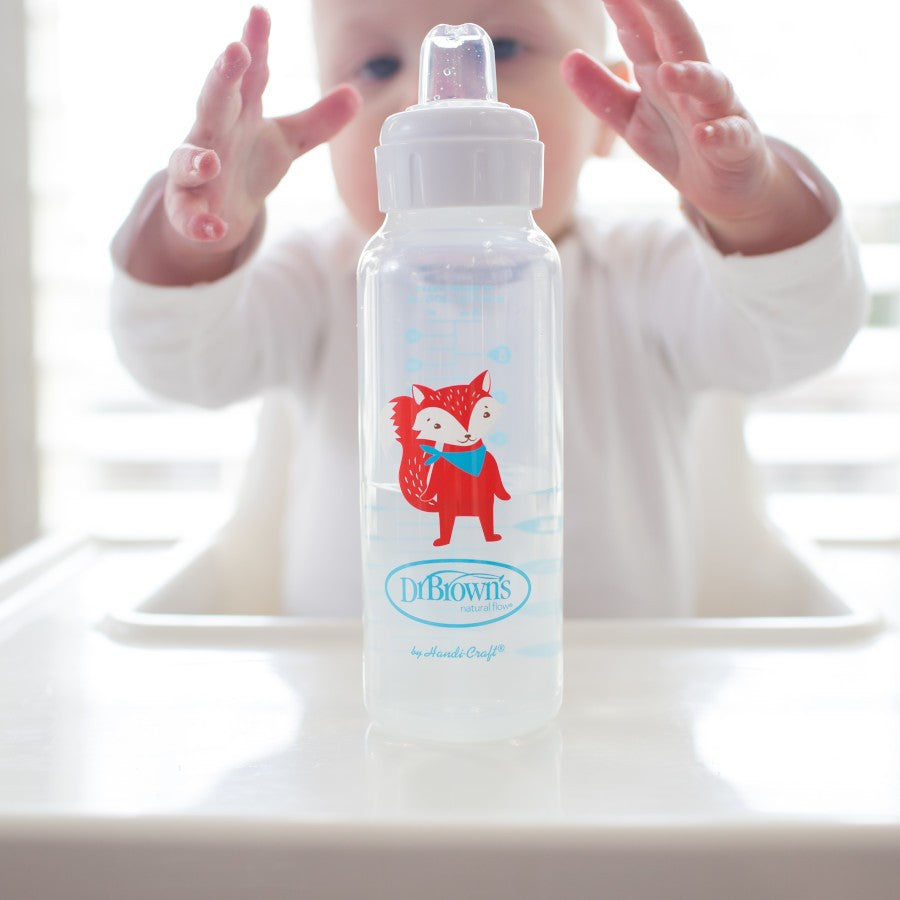 A baby reaching for a clear baby bottle with a red fox illustration and "Dr. Brown's" written on it, sitting on a white high chair tray.