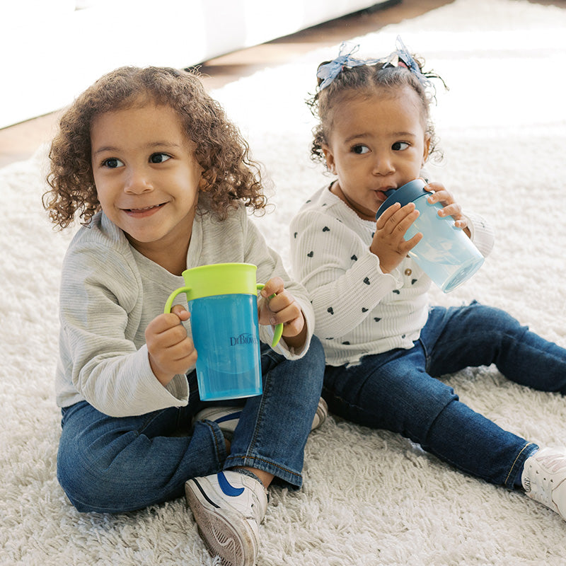 Two kids sitting on a white rug drinking from Dr. Brown's cups Straw to 360 cups.