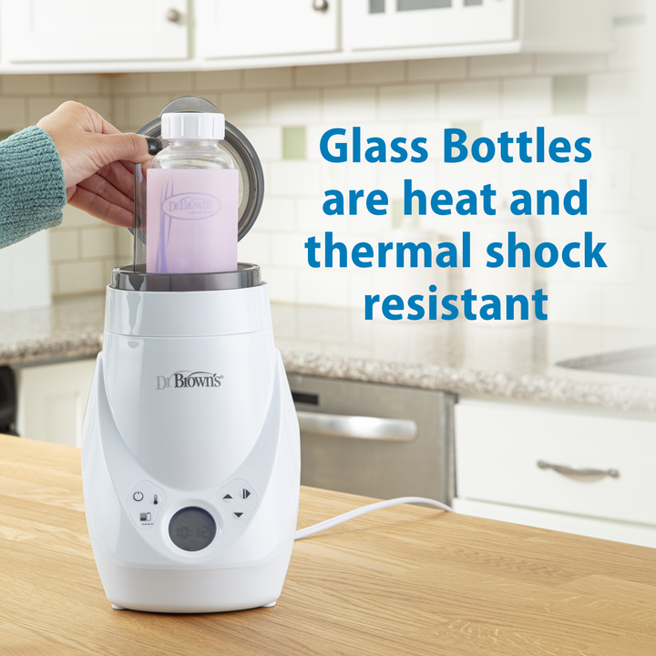 Dr. Brown's bottle warmer with a glass bottle on a kitchen counter, text about heat and thermal shock resistance.
