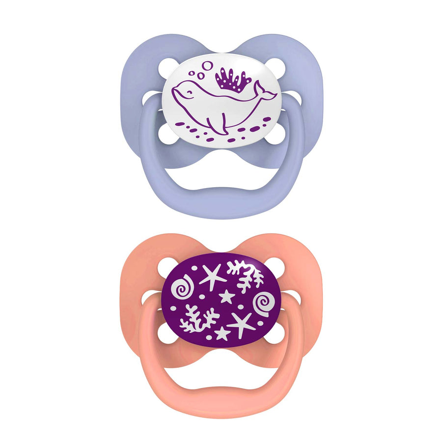 Dr. Brown's™ Advantage™ Glow-in-the-Dark Pacifiers, 2 Count features two baby pacifiers: a top one with a light purple shield and whale design that glows, and a bottom one with a peach shield adorned with starfish and seashells on a white background with purple illustrations.