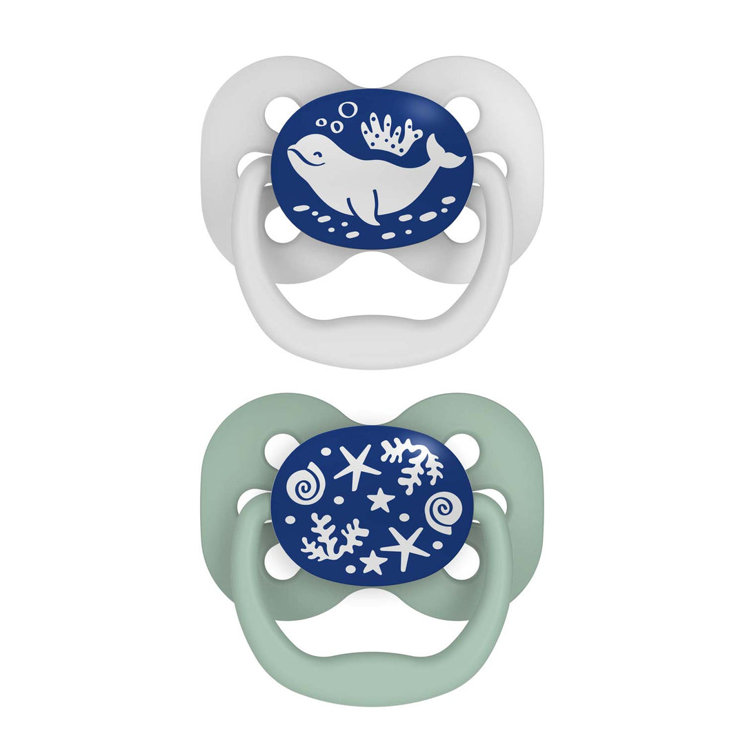 Dr. Brown's™ Advantage™ Glow-in-the-Dark Pacifiers, 2 Count, feature nautical designs: a white with blue shield and whale pacifier, and a light green with a blue shield displaying seashells and starfish pacifier. These symmetrical soothers ensure your baby's comfort.