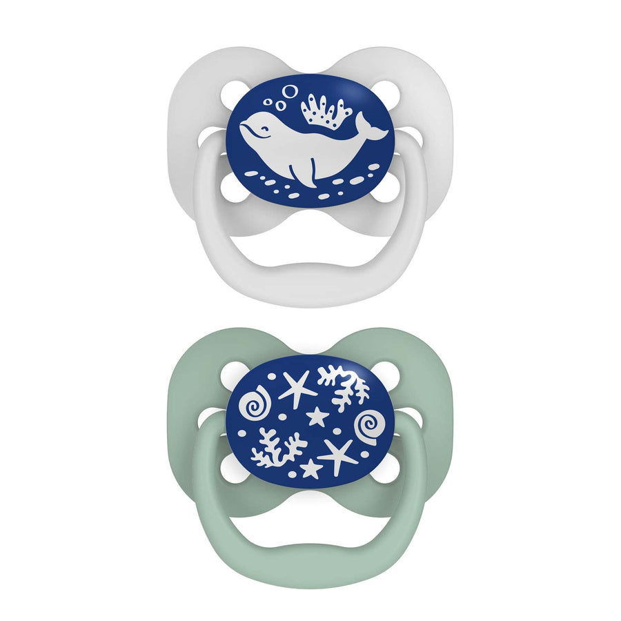 Dr. Brown's™ Advantage™ Glow-in-the-Dark Pacifiers, 2 Count, feature nautical designs: a white with blue shield and whale pacifier, and a light green with a blue shield displaying seashells and starfish pacifier. These symmetrical soothers ensure your baby's comfort.