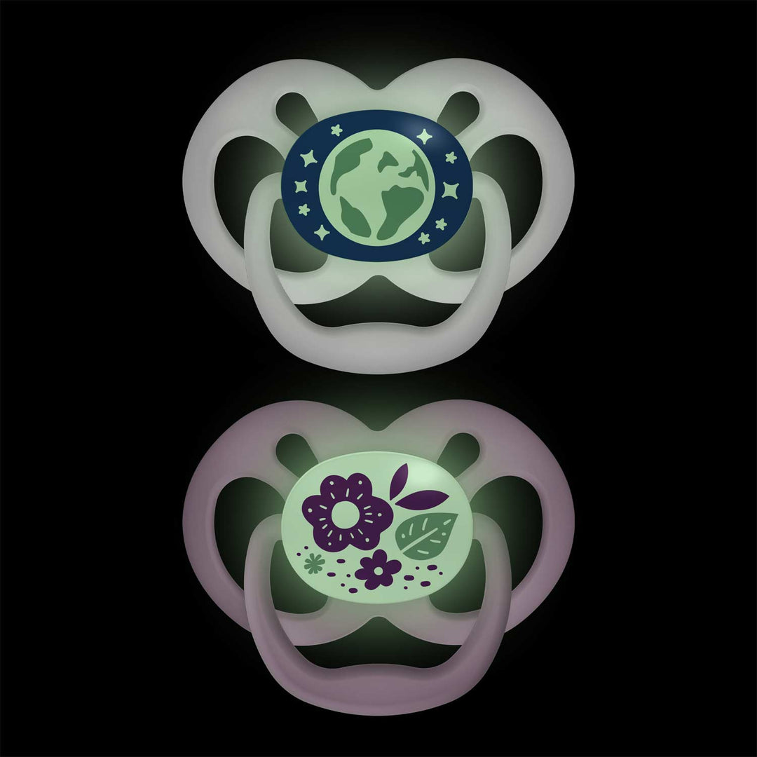 On a black background, Dr. Brown's™ Advantage™ Glow-in-the-Dark Pacifiers feature one with an Earth and stars design on blue-green, and another with purple flowers and green leaves. Both include convenient reversible bulbs.