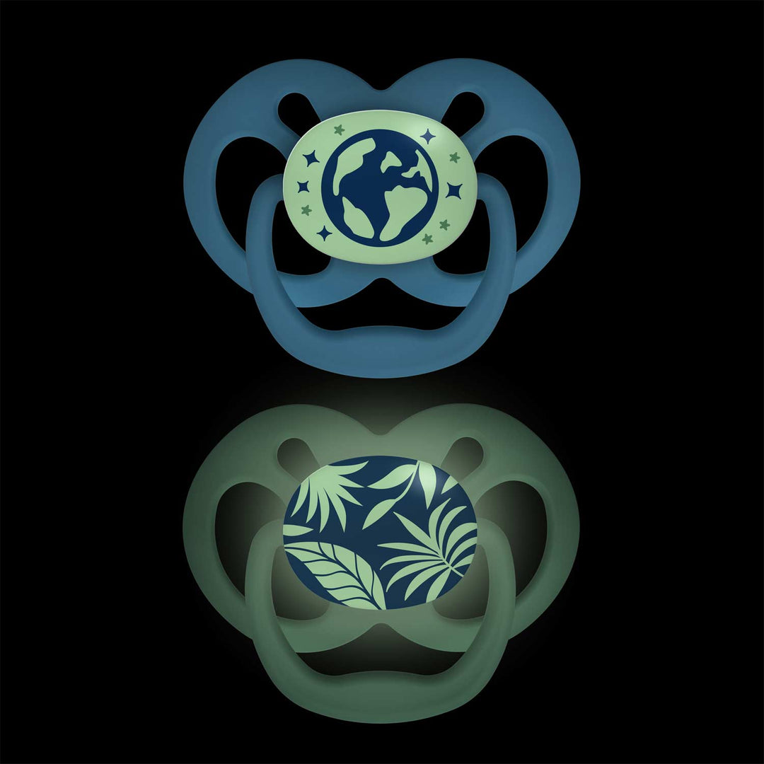 Dr. Brown's™ Advantage™ Glow-in-the-Dark Pacifiers, 2 Count, features two attention-grabbing designs on a black background: a glowing globe motif with stars and a symmetrical dark green soother adorned with green leaves.