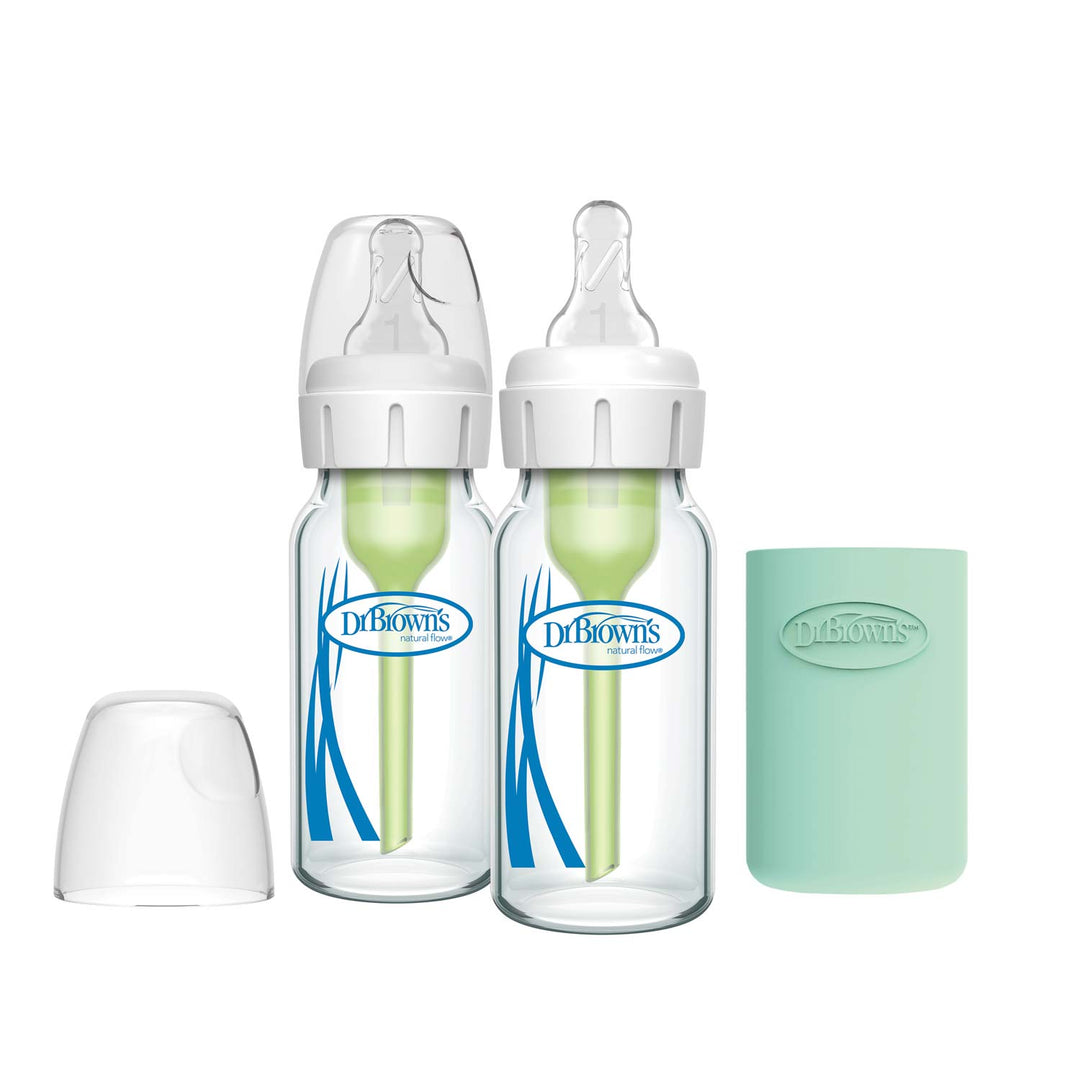 Two Dr. Brown’s Natural Flow® Anti-Colic Options+™ Narrow Glass Baby Bottles with silicone sleeves and clear lids sit side by side, with a separate clear cap and a mint-green sleeve to the right.