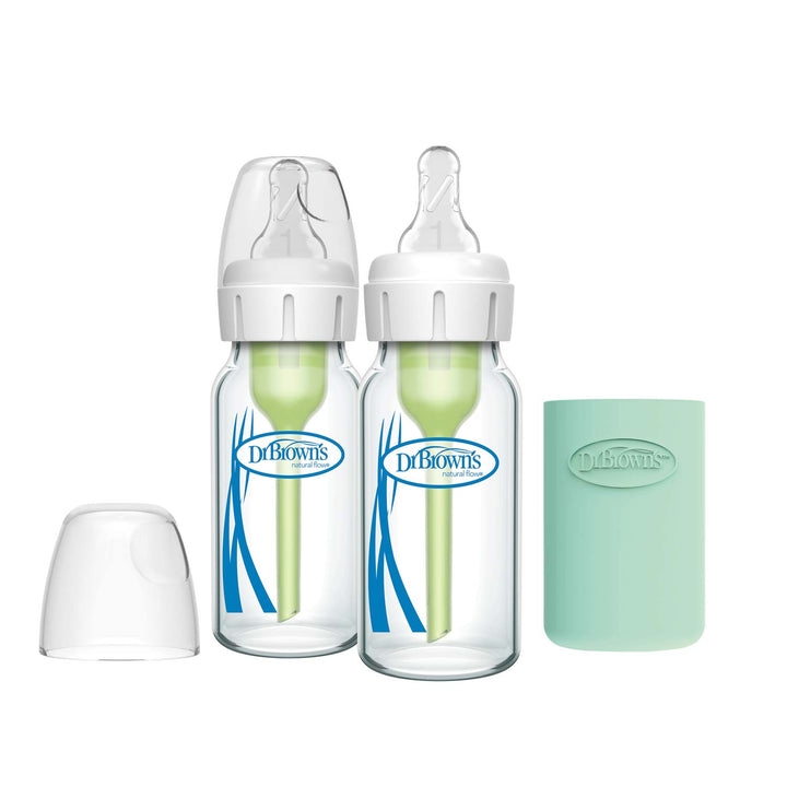 Two Dr. Brown’s Natural Flow® Anti-Colic Options+™ Narrow Glass Baby Bottles with silicone sleeves and clear lids sit side by side, with a separate clear cap and a mint-green sleeve to the right.