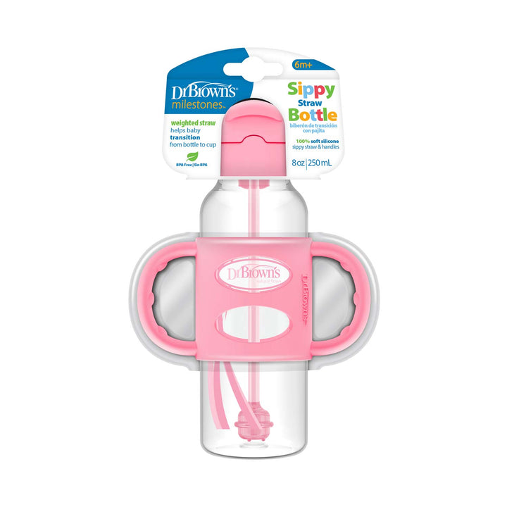 The packaging of Dr. Brown’s™ Milestones™ Narrow Sippy Straw Bottle with Silicone Handles, 8 oz/250 mL, highlights its pink handles and cap. Equipped with a flip-to-sip lid and a silicone weighted straw, it is ideal for fostering independent drinking skills in children aged 6 months and older.