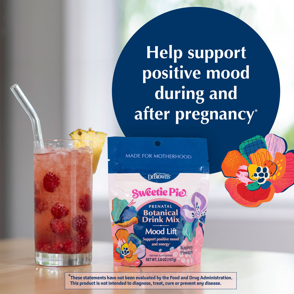 A package of Dr. Brown's Sweetie Pie Prenatal Botanical Drink Mix is displayed on a table next to a glass of pink raspberry iced tea with a straw and a pineapple wedge.
