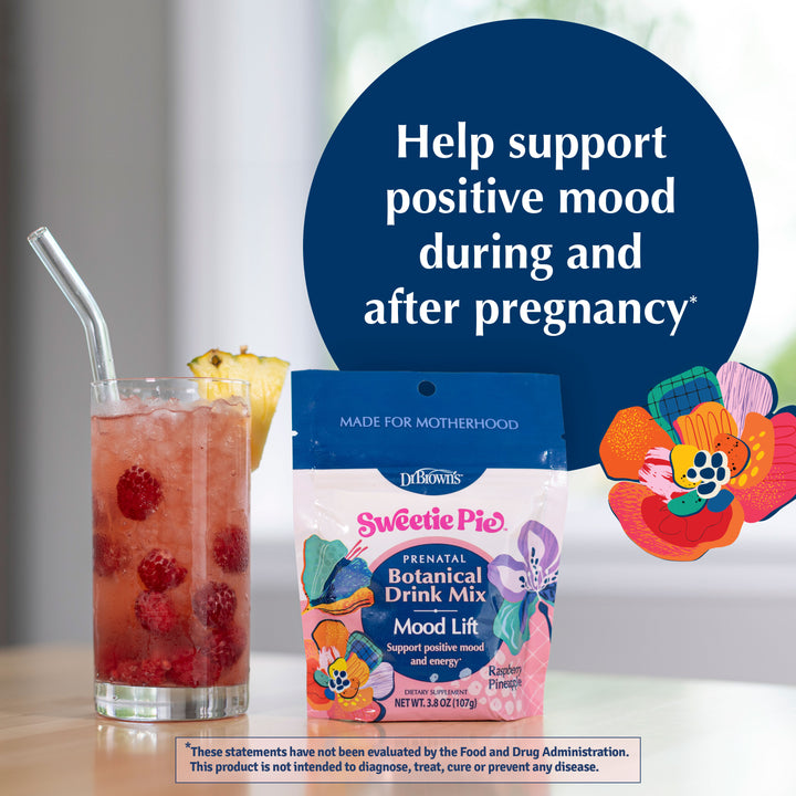 A package of Dr. Brown's Sweetie Pie Prenatal Botanical Drink Mix is displayed on a table next to a glass of pink raspberry iced tea with a straw and a pineapple wedge.
