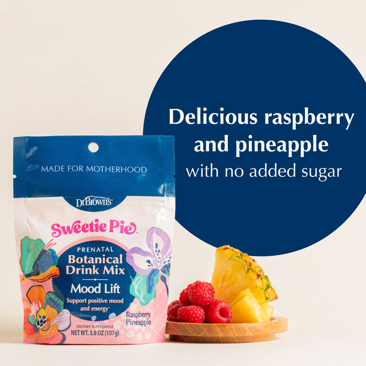 A bag of Dr. Brown's Sweetie Pie Raspberry Pineapple botanical drink mix is shown next to a wooden bowl of fresh raspberries and pineapple slices, with a large blue circle containing the text 'Delicious raspberry and pineapple with no added sugar'.