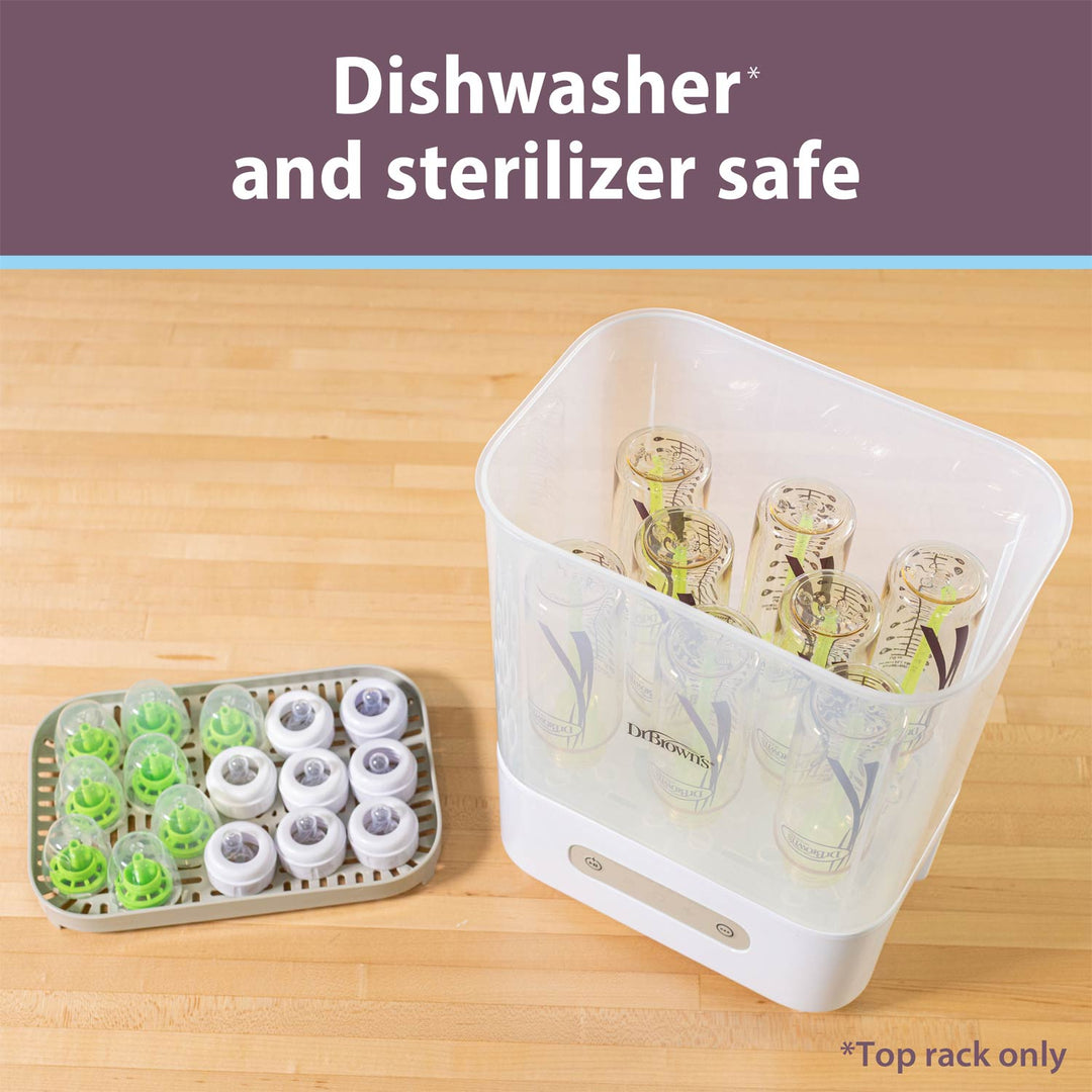 A white and clear dishwasher and sterilizer safe baby bottle warmer shown on a light wood surface, with a tray of detachable green and white dishwasher-safe inserts beside it. Text at the top reads 'Dishwasher and sterilizer safe'.