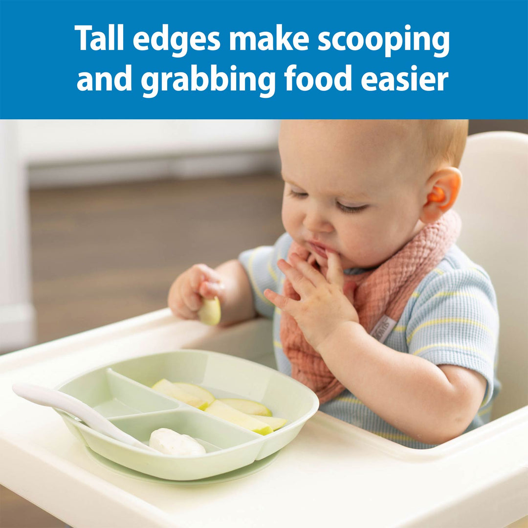 A baby seated in a high chair using a mint No-Slip Divided Suction Plate with a spoon on the tray. A blue banner at the top reads, 'Tall edges make scooping and grabbing food easier.
