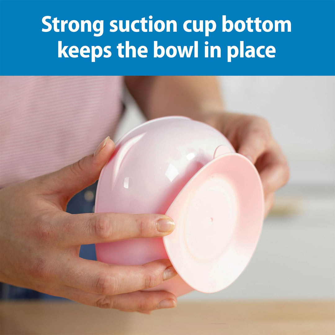 A person holds a light pink suction cup bowl, demonstrating its strong suction base. A blue banner at the top contains white text that reads 'Strong suction cup bottom keeps the bowl in place'.