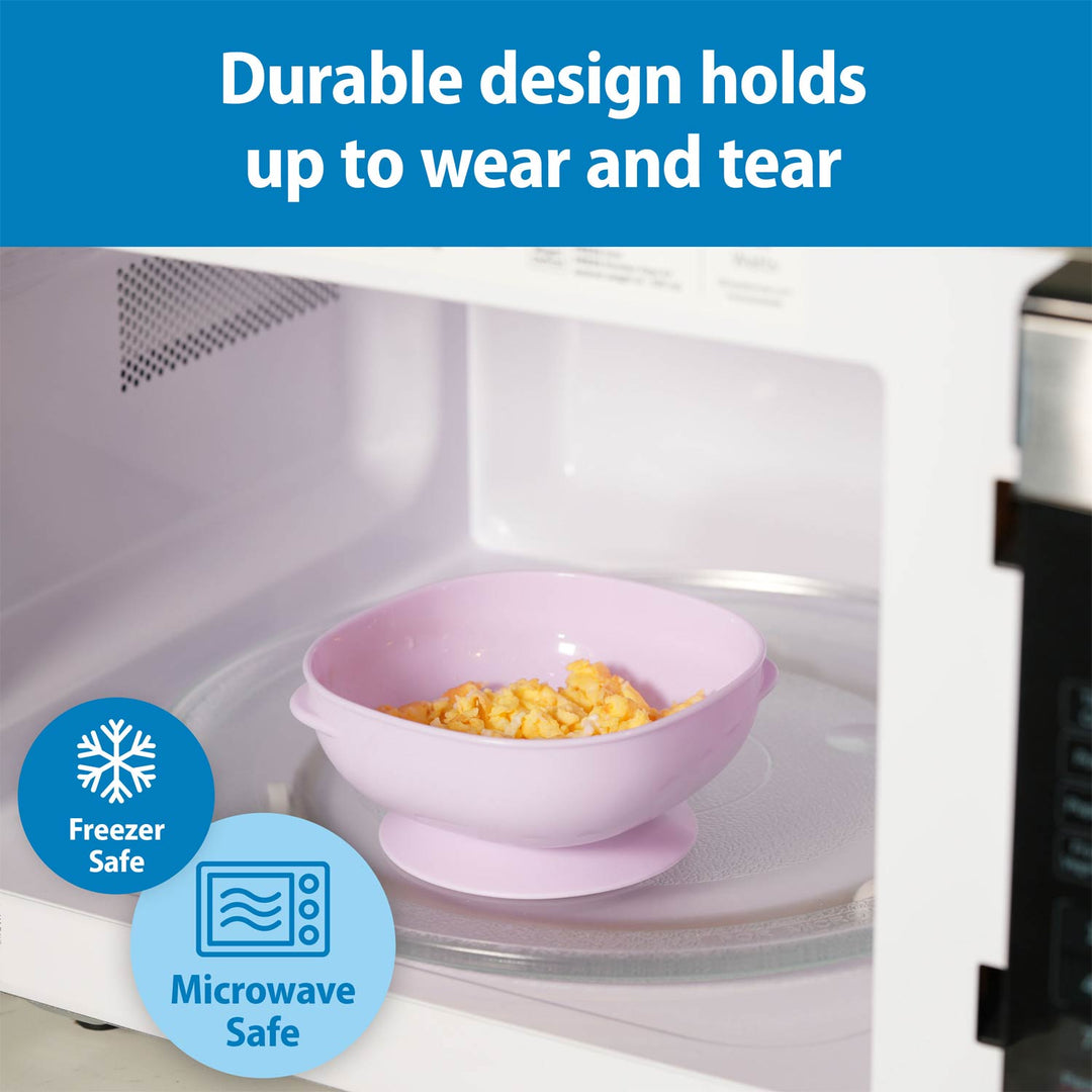A pink silicone bowl with a suction base sits inside a white microwave, with corn on a glass turntable. A blue banner at the top reads 'Durable design holds up to wear and tear,' and blue circular badges at the bottom left say 'Freezer Safe' and 'Microwave Safe.