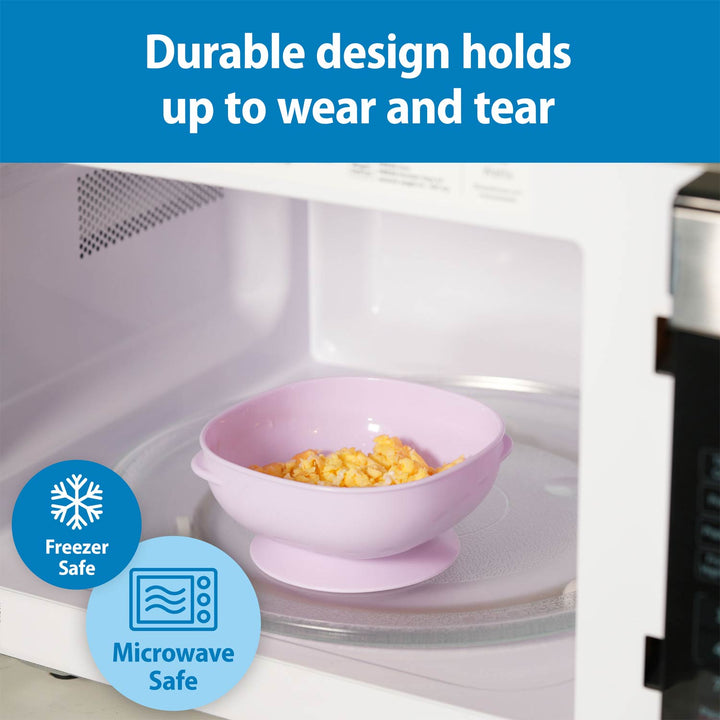 A pink silicone bowl with a suction base sits inside a white microwave, with corn on a glass turntable. A blue banner at the top reads 'Durable design holds up to wear and tear,' and blue circular badges at the bottom left say 'Freezer Safe' and 'Microwave Safe.