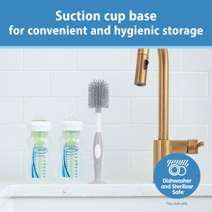 Bottle and brush set with suction cup base on a kitchen sink, featuring a gold faucet.